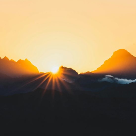 Sun setting behind mountains, creating a beautiful glow.