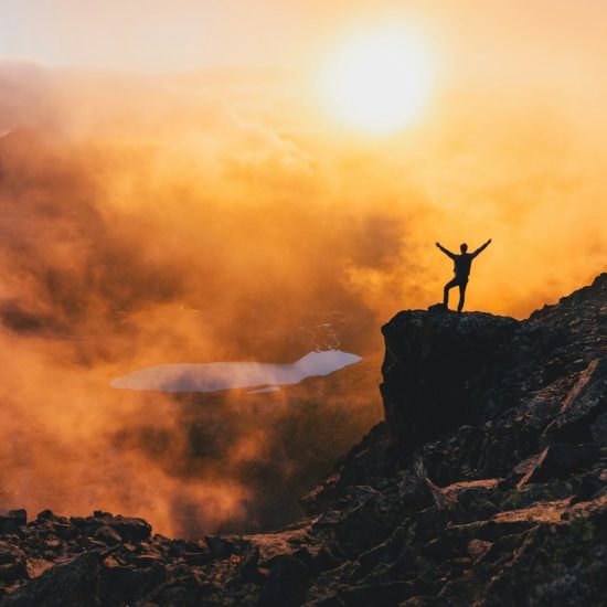 Man stands triumphant on a mountain in sunset.