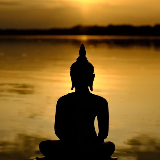 a buddha statue sitting in front of a body of water